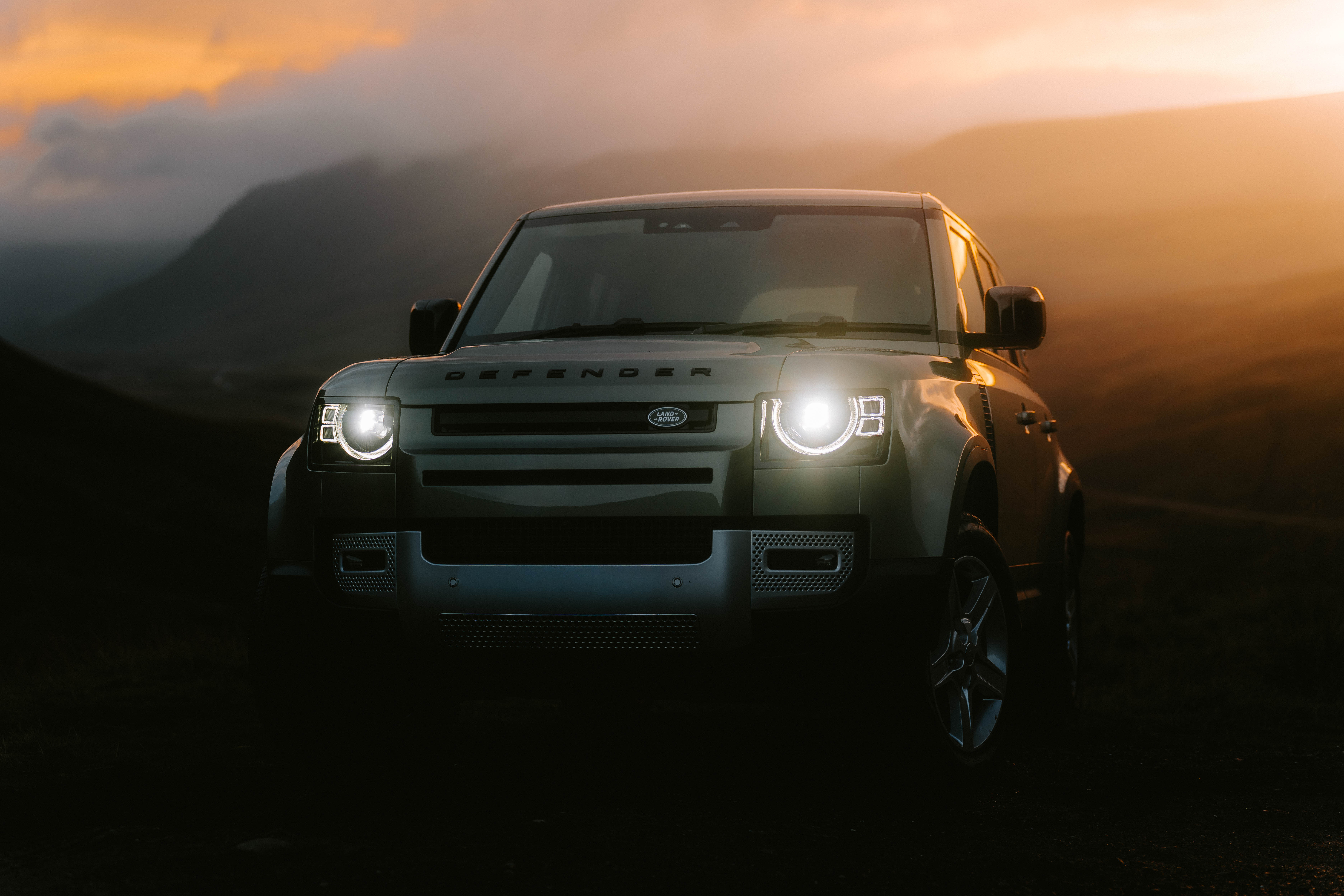 A silver Land Rover Defender with a misty sunset background